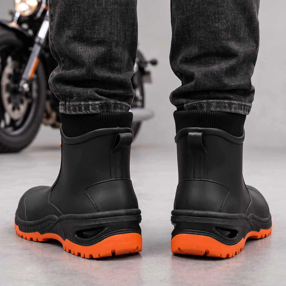 Schwarze Gummistiefel mit orangefarbener Sohle zu dunkler Jeans, Ansicht von hinten mit Anziehlaschen.
