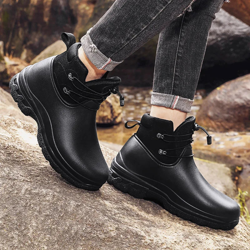 Schwarzer Gummistiefel mit Schnürzug, getragen von Person auf Felsen | Chaps Herrenmode