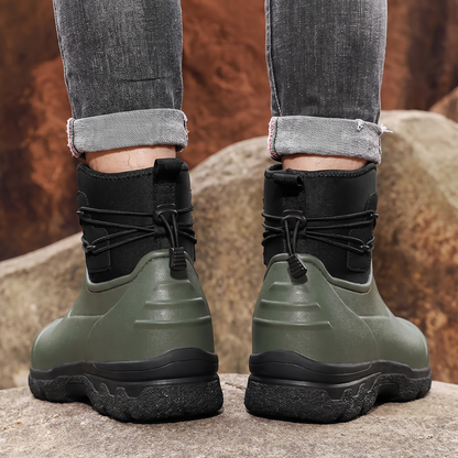 Grüne Gummistiefel mit schwarzem Schaft, getragen an Beinen vor Felsen | Chaps Herrenmode