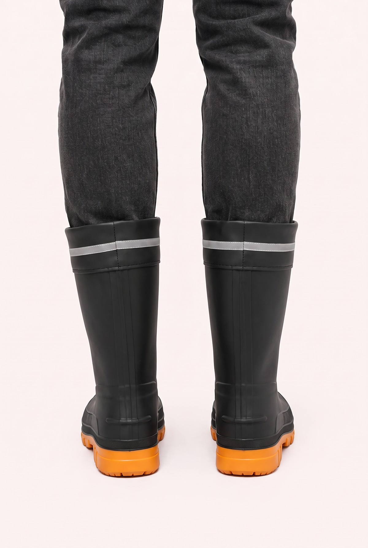 Schwarze Gummistiefel mit orangefarbener Sohle, getragen an den Beinen einer Person | Chaps Herrenmode