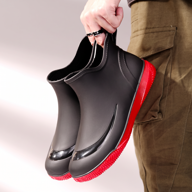 Hand hält ein Paar schwarze Gummistiefel mit roter Sohle, Seitenansicht