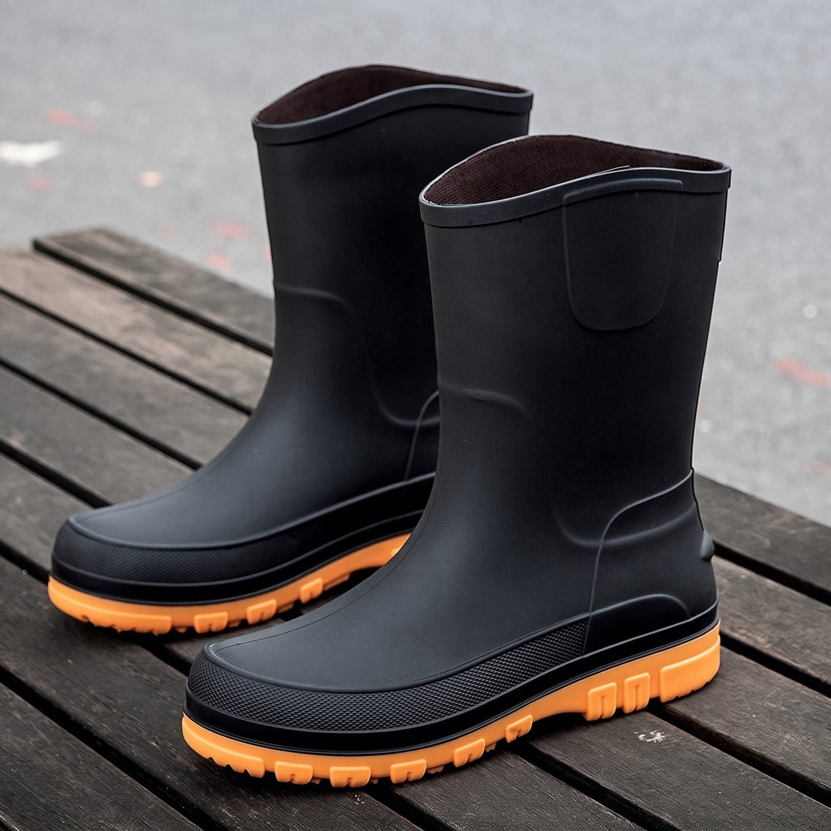 Schwarze Gummistiefel mit orangefarbener Sohle, freistehend auf Holzuntergrund fotografiert | Chaps Herrenmode