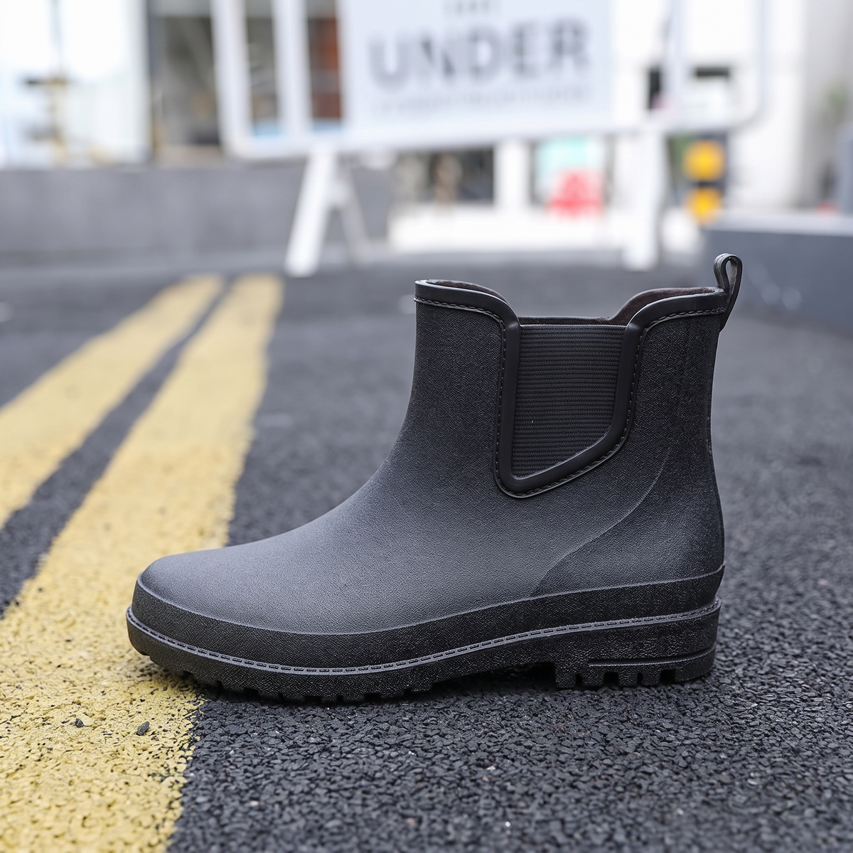 Schwarzer Chelsea-Gummistiefel für Herren in der Seitenansicht, auf Asphalt neben gelber Fahrbahnmarkierung