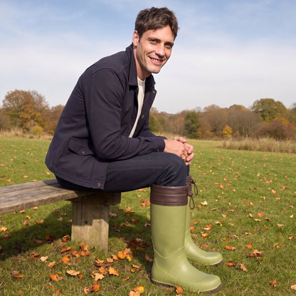 Olivgrüne Gummistiefel mit brauner Stulpe, getragen von einem sitzenden Mann im Freien | Chaps Herrenmode