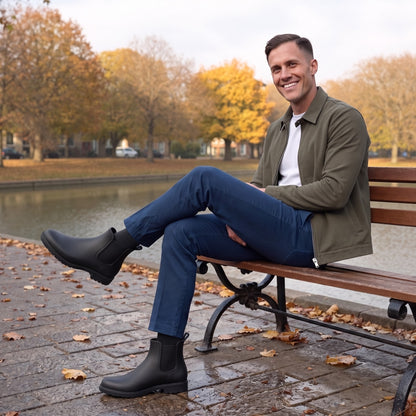 Mann sitzt auf einer Parkbank am Kanal und trägt schwarze Chelsea-Gummistiefel