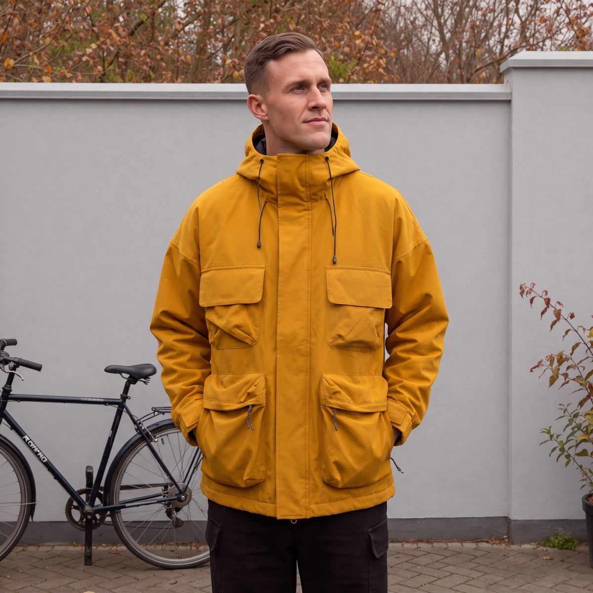 Model trägt die senfgelbe Utility-Regenjacke für Herren mit Kapuze