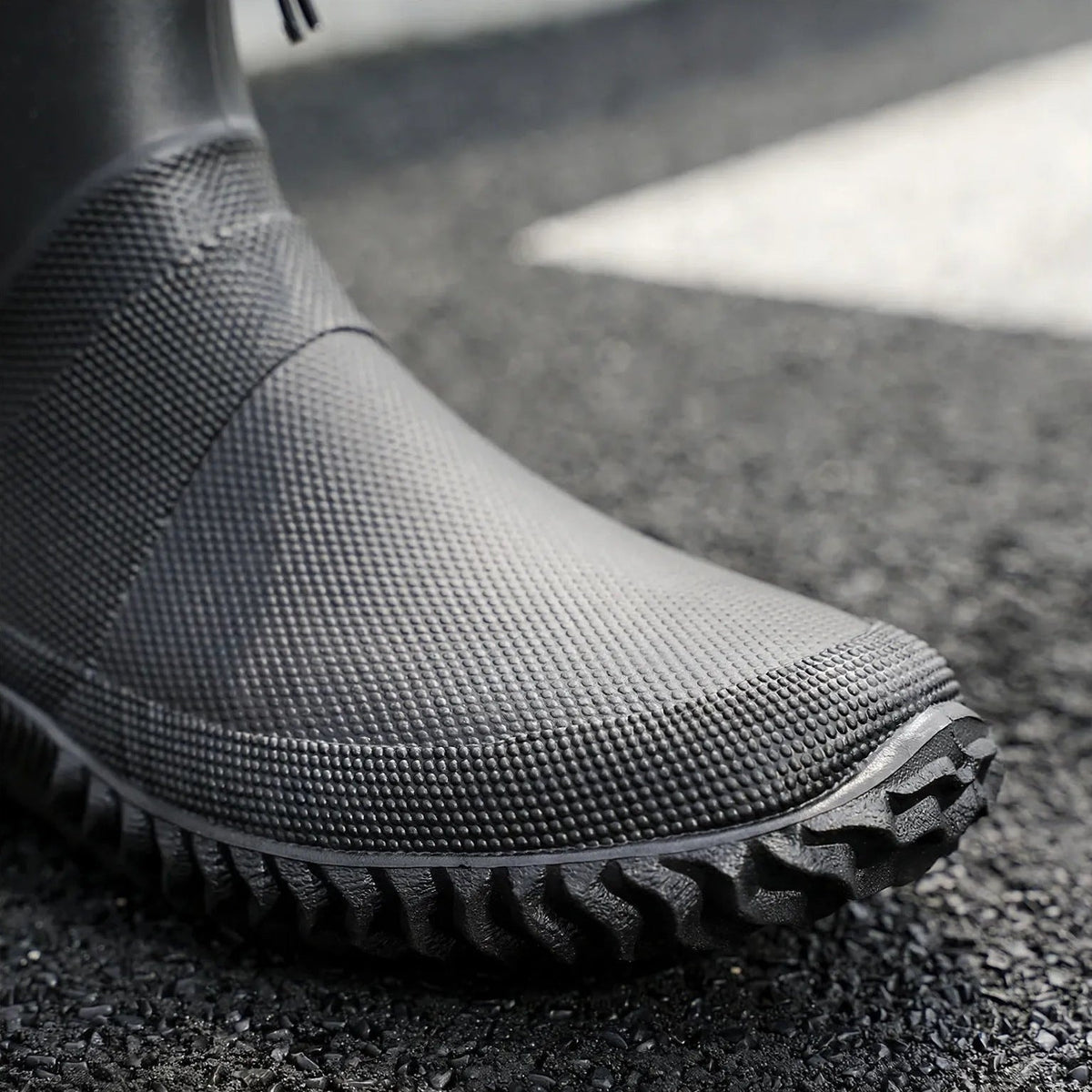 Schwarzer Gummistiefel mit Profilsohle, getragen, Nahaufnahme auf Asphalt | Chaps Herrenmode