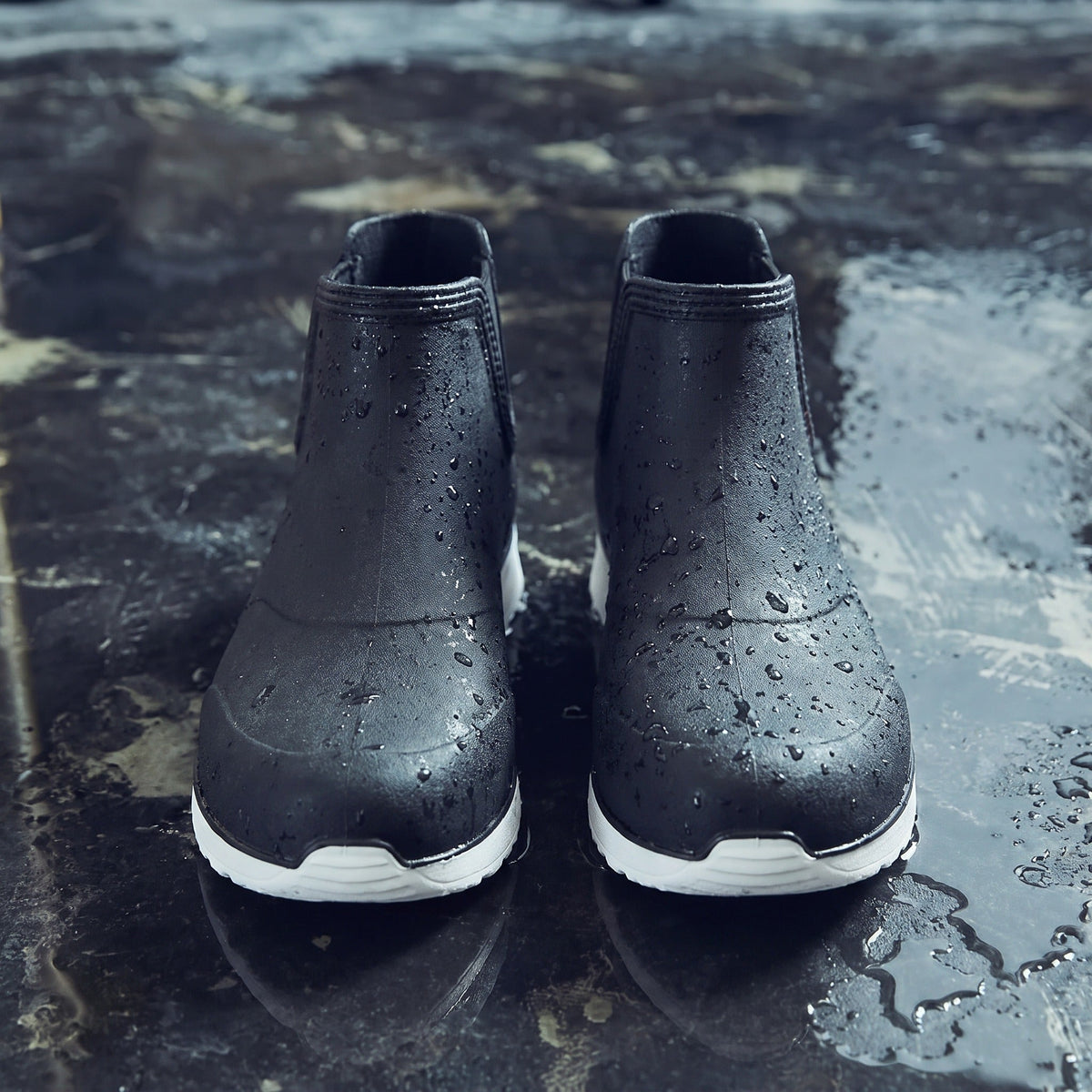 Schwarze Chelsea-Regenstiefel mit weißer Sohle, nass, auf regennasser Fläche stehend | Chaps Herrenmode