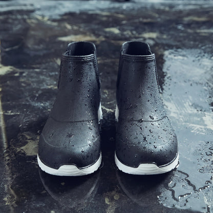 Schwarze Chelsea-Regenstiefel mit weißer Sohle, nass, auf regennasser Fläche stehend | Chaps Herrenmode