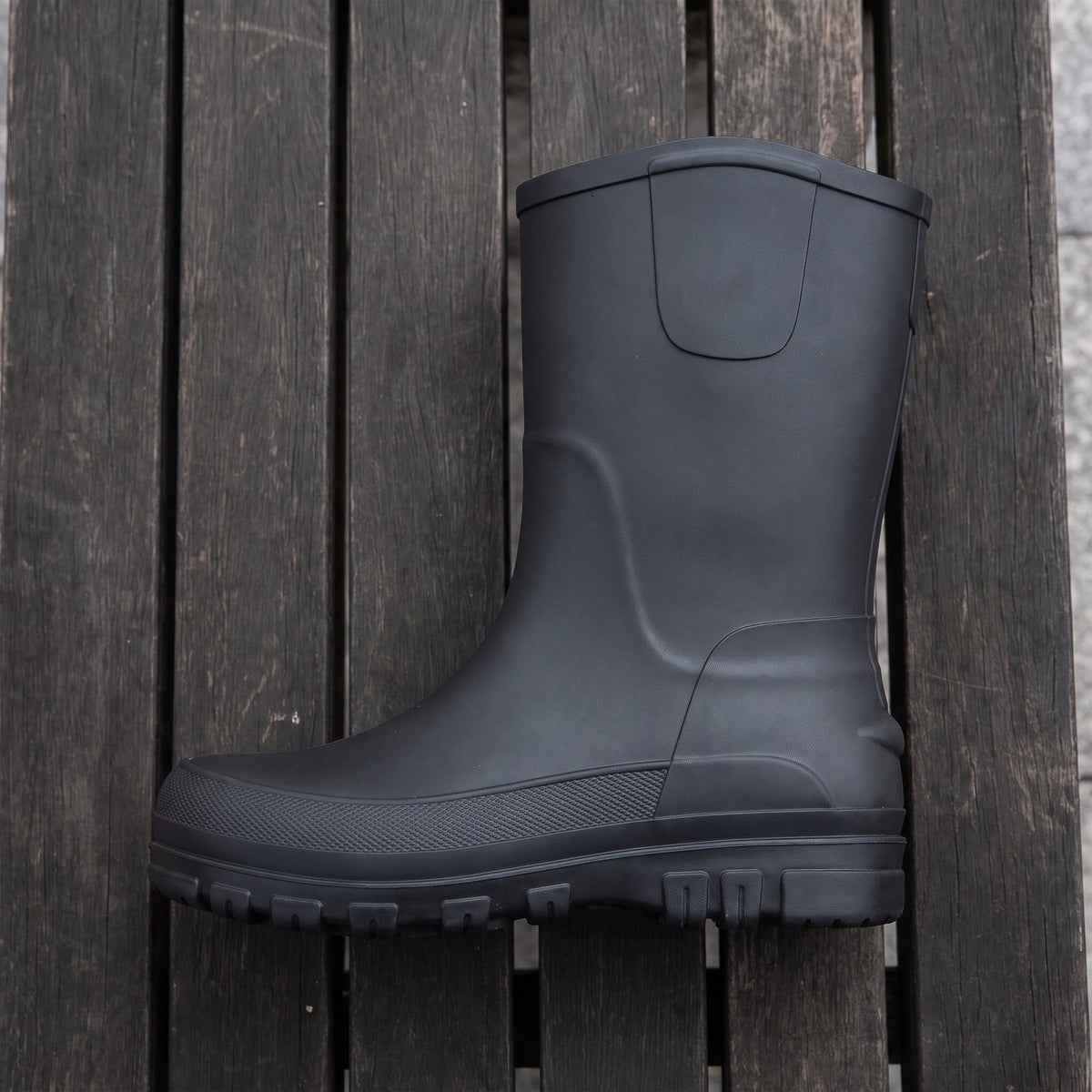 Schwarzer halbhoher Gummistiefel mit Profilsohle, freigestellt auf Holzuntergrund fotografiert | Chaps Herrenmode