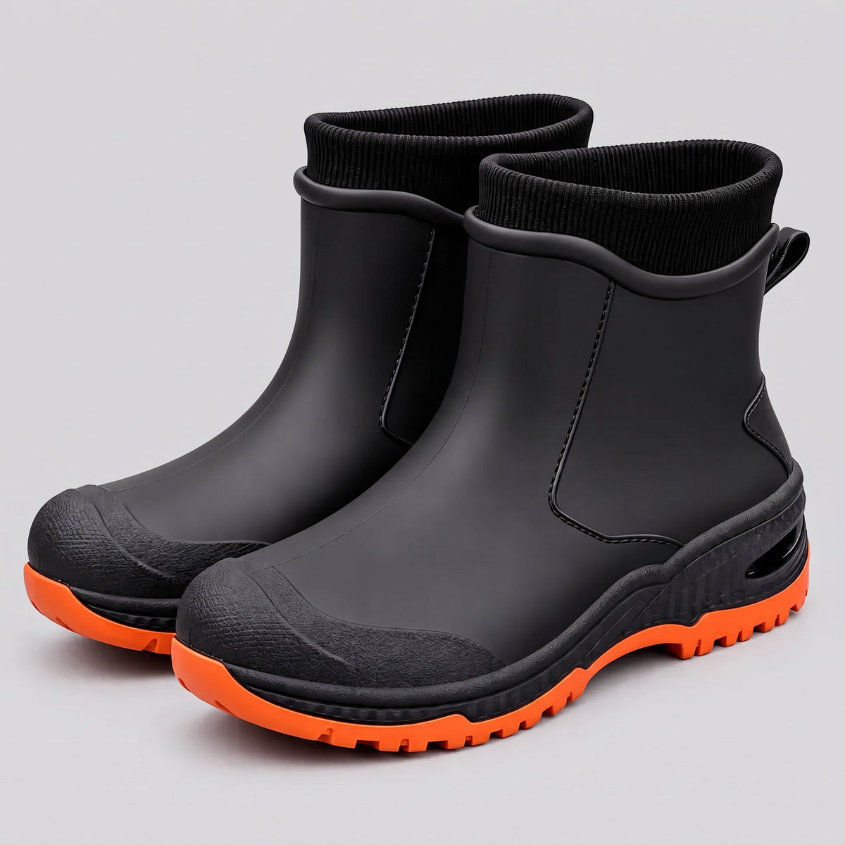 Schwarze knöchelhohe Gummistiefel mit orangefarbener Profilsohle und gerippten Strickbündchen, Studioaufnahme.